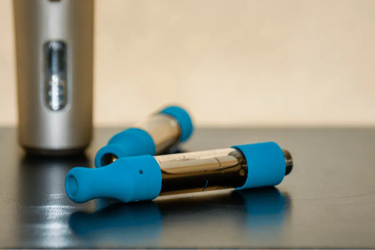 two vape cartridges with blue mouthpieces beside a battery