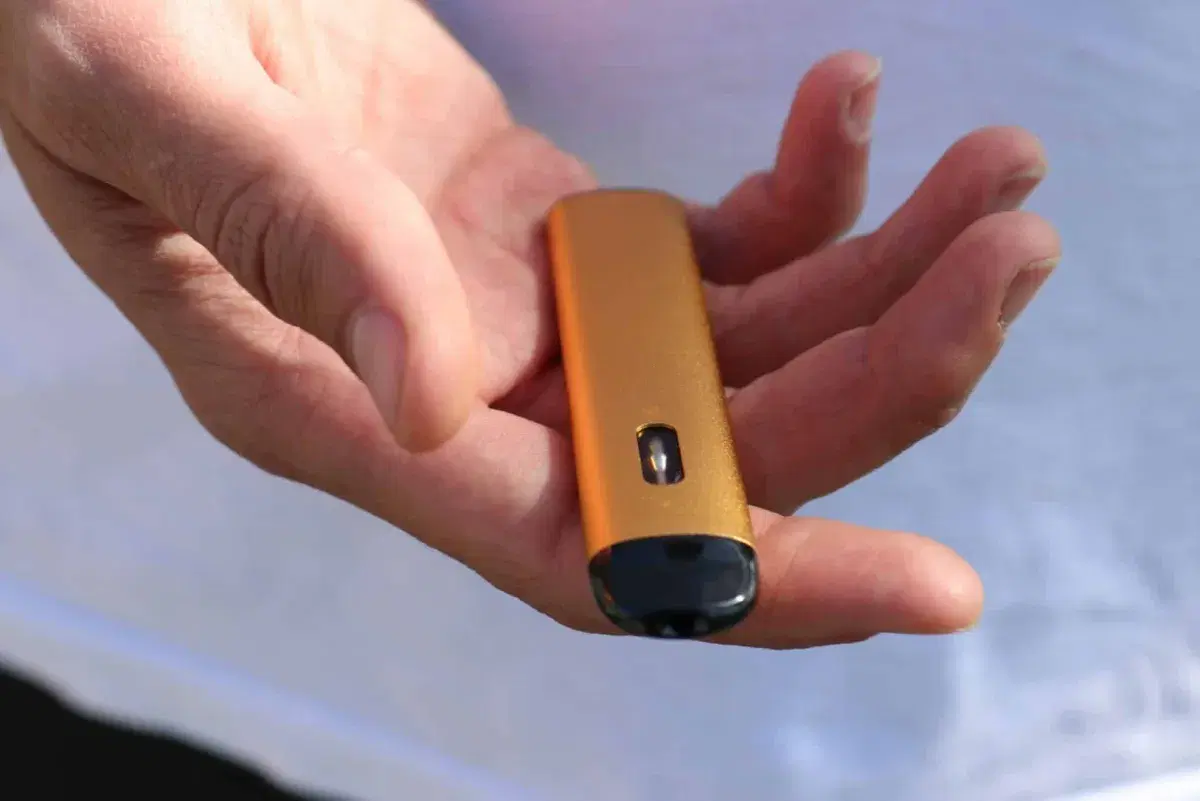 a hand holding an orange disposable vape