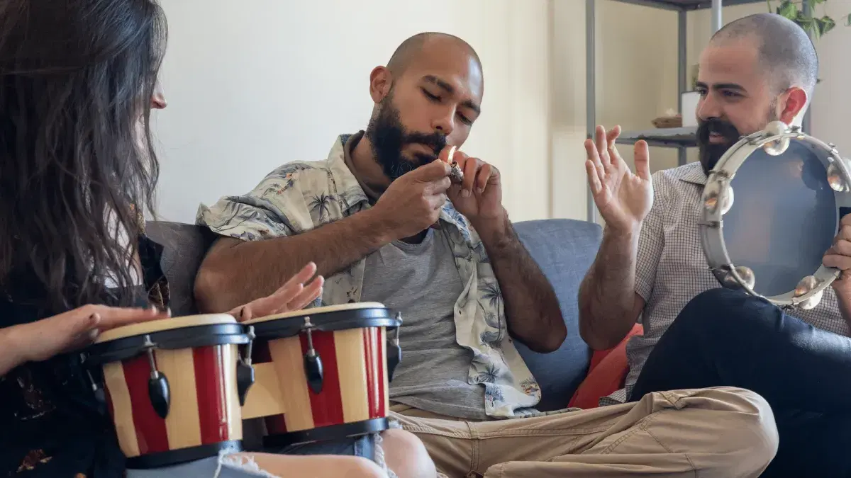friends playing bongo drums and smoking on a sofa